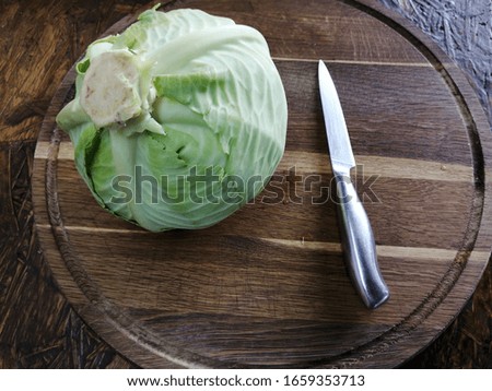 A whole head of fresh white cabbage with a knife for making salad on a wooden board