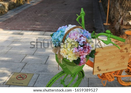 There is a green bicycle standing on the street. And the basket is full of flowers.