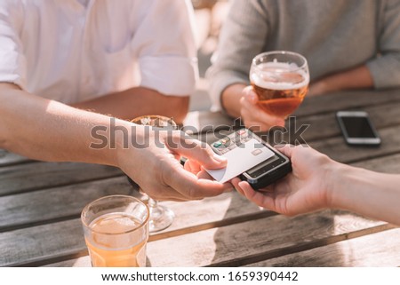 Close-up of male hand paying at restaurant with credit card - lifestyle picture of people relaxing at brewery and paying with plastic card at the table