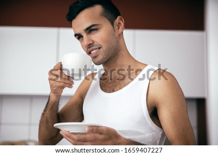 Happy handsome guy in t-shirt drinking coffee at the kitchen in the morning stock photo