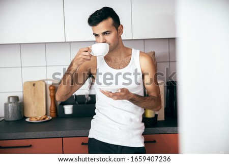 Waist up of handsome man in white t-shirt holding hot drink at the kitchen stock photo