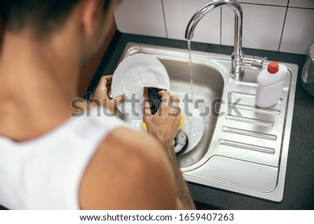 Top view of young man in t-shirt washing dishes in the kitchen stock photo