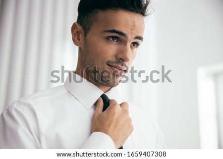 Happy man in shirt dressing up and adjusting tie on neck at home stock photo