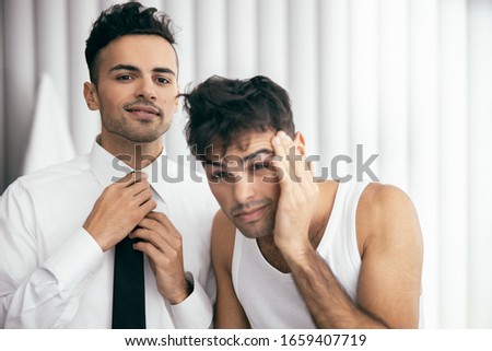 Handsome man adjusting tie with his young brother in t-shirt near him stock photo