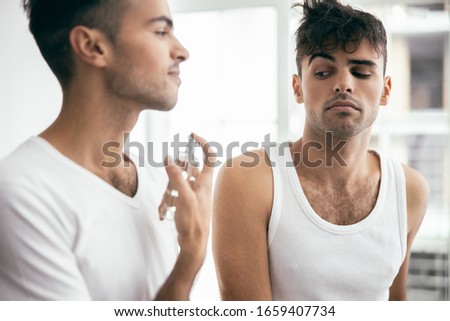 Happy handsome male spraying perfumes while his brother standing near him in room stock photo