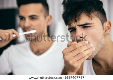 Cropped photo of guy checking breath while his brother using toothbrush next to him stock photo