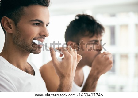 Cropped photo of young guy using toothbrush while his brother standing next to him stock photo
