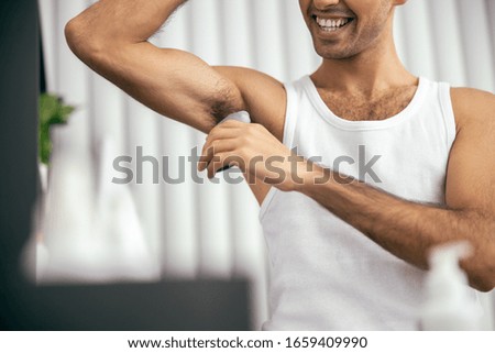 Cropped photo of happy guy applying deodorant to armpit at home stock photo