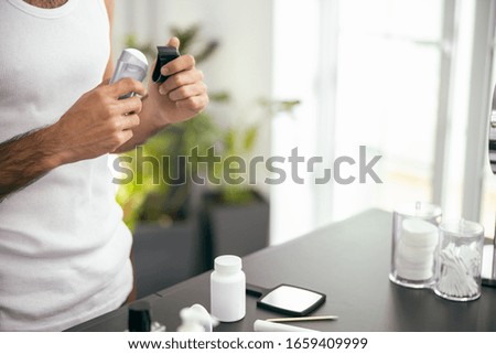 Cropped photo of young man in white t-shirt holding antiperspirant while opening it stock photo