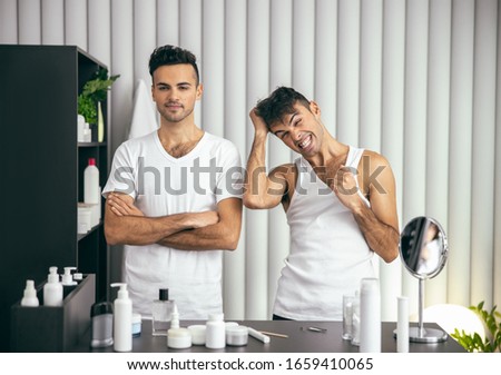 Waist up of handsome twins posing near table with cosmetics at home stock photo