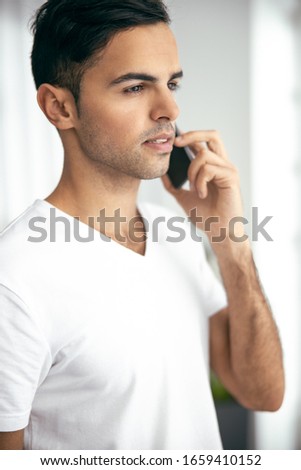 Close up of handsome guy using mobile phone in his flat stock photo