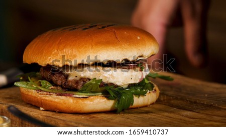 Close up of home made tasty burger on wooden table, gastronomy and foodporn concept. Stock footage. Juicy sandwich with beef, cheese, lettuce and onion.