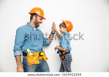 Happy dad and little boy in helmets and belts with instruments are taking five together. Isolated on white background Royalty-Free Stock Photo #1659412294