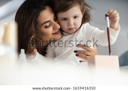 happy young mother standing near her daughter while doing makeup at home stock photo