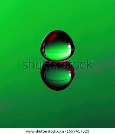 Macro photograph of a Water drop at impact with water on green background.