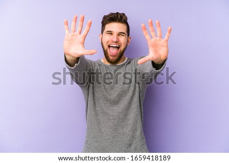 Young caucasian man isolated on purple background showing number ten with hands.