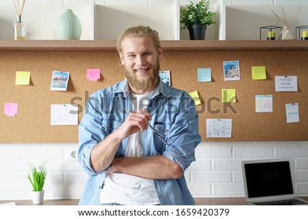 Smiling confident millennial hipster man look at camera standing posing at workspace with sticky notes mood board, happy male student, creative occupation professional designer freelancer portrait