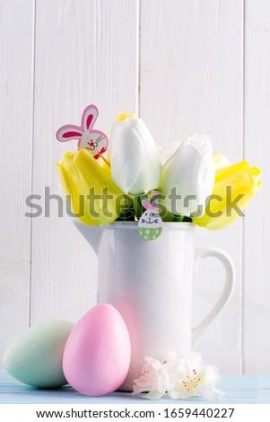 Congratulation Easter card with fresh tulips, handmade painted eggs and decotation against light grey wooden background.