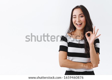 Cheeky feminine asian girlfriend keep everything under control, standing relaxed and chill with no worries, showing okay, confirmation or approval gesture, wink hinting and smiling, white background