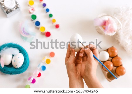 Child's hands coloring easter eggs with colors and brush on light background. Easter, holidays, tradition concept