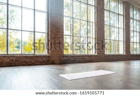 White mat on wooden floor empty modern spacious gym private fitness classroom sport club studio class training daylight big windows with brick walls workout yoga healthy lifestyle concept copy space. Royalty-Free Stock Photo #1659505771
