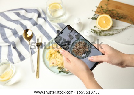 Food blogger taking picture of tasty pasta with shrimps and tomatoes at light table, closeup
