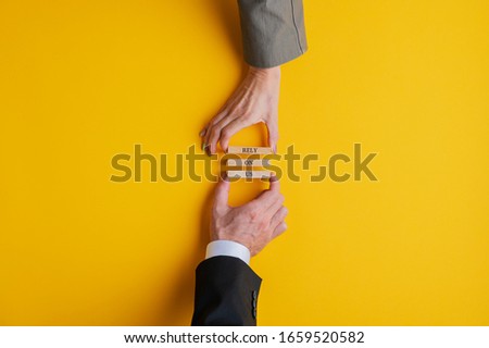 Businessman and businesswoman working as a team to make a Rely on us sign spelled on wooden pegs. Over yellow background with copy space.