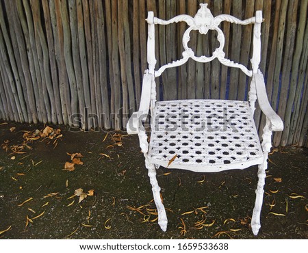 WHITE CAST IRON CHAIR IN FRONT OF A WOODEN POLE SCREEN                               