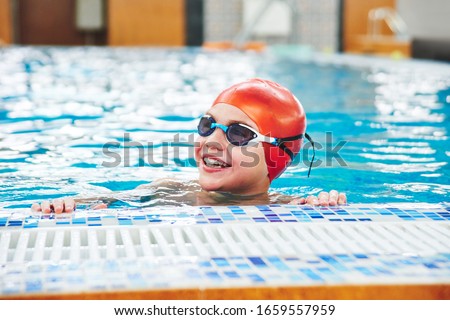 Joyful smiling boy swimmer in a cap and Goggles learns professional swimming in the swimming pool in gym close up