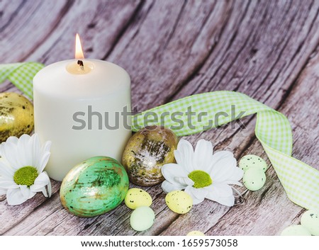 Easter eggs in nest with candle and flowers on rustic wooden background