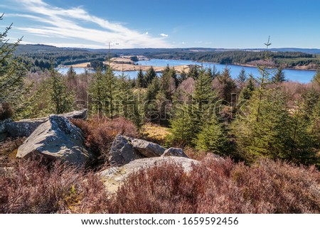 Kielder Forest / Kielder Reservoir in Northumberland. High on the rocks looking over the tree-tops towards the reservoir. Kielder dam is known for its hydroelectric plant, opened in 1972. Royalty-Free Stock Photo #1659592456