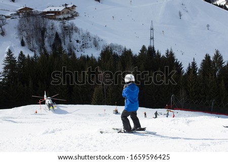 Child, watching rescue action on ski slope, helicopter picking up injured person from ski slope in Austria