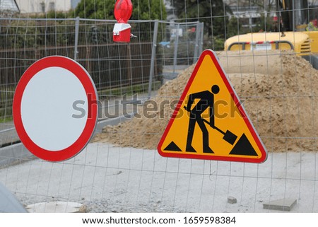 Road works warning sign and no entry hanging on the fence in front of a road construction site in Poland.