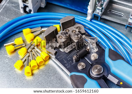 Wire stripper with unused yellow cord end insulated ferrules and blue stranded wire on metal mounting plate close-up Royalty-Free Stock Photo #1659612160