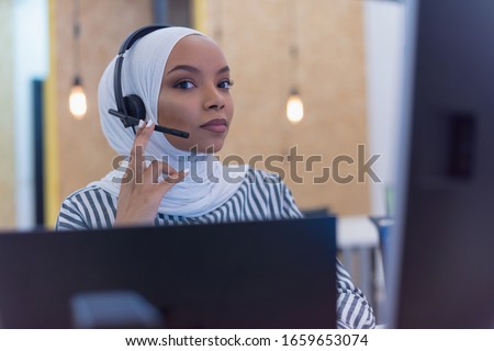 Happy african muslim woman in call center. Female Customer Service Representative Answer Client's Questions in a Headset. Multi-Ethnic Team of Specialists.
