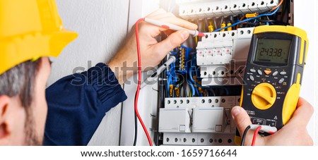 Electrician installing electric cable wires and fuse switch box. Multimeter in hands of electricians detail. Royalty-Free Stock Photo #1659716644