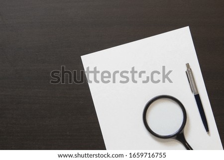 Template of white paper with pen and magnifier on dark wenge color wooden background. Concept of business plans, searching, detecting and solving problems. Stock photo with empty space for text.