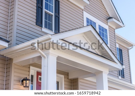 Portico leading to the entrance of vinyl horizontal lap siding covered building, with a roof structure over a walkway, supported by white rectangular columns on a new single family home in Maryland Royalty-Free Stock Photo #1659718942