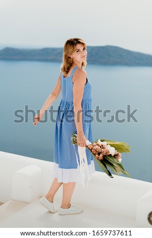 Beautiful girl walking with bouquet of flowers along the street of Santorini island, an old European town, Greece. Portrait of a tourist girl walking on the street background. Love story summer