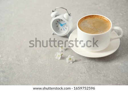 Cup of morning coffee, flowers and alarm clock on light grey table. Space for text