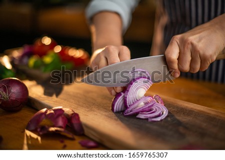 Female chef is precisely slicing red onions on a wooden cutting board in a restaurant.  Royalty-Free Stock Photo #1659765307