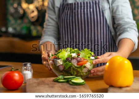 Female chef presenting a glass bowl of freshly made healthy vegetable salad in a rustic type kitchen. 