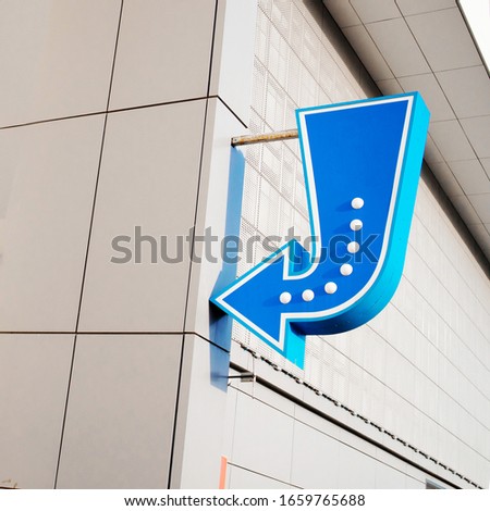 Blue arrow sign with light bulbs on the wall. Direction the way. 
