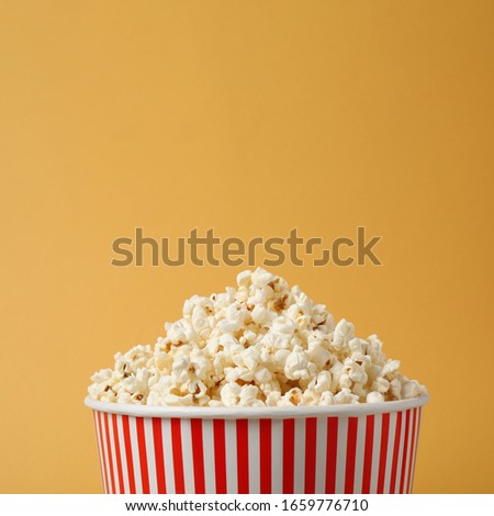 Delicious popcorn in paper bucket on yellow background, closeup