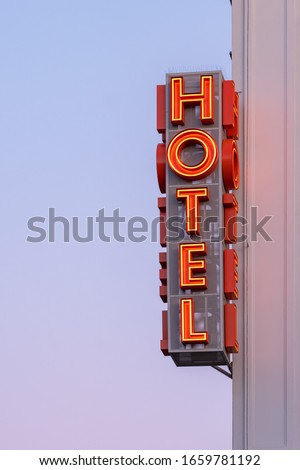 Neon hotel sign on the building corner against the sunset sky Empty copy space for inscription. Vintage sign. Vertical hotel sign
