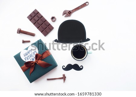 
Father's Day Holiday Concept. Flatlay. Hat, coffee mug, gift, chocolates in the form of old tools and a funny black mustache on an isolated white background. Copy space for inscriptions.