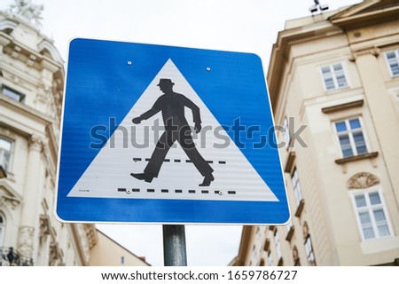 crosswalk sign, blue pedestrian symbol in front of buildings in Vienna, Austria