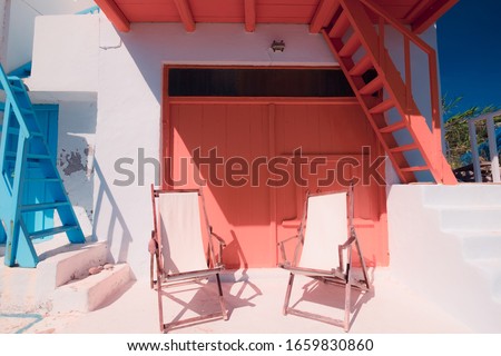 Beach chairs for relaxation near traditional colorful greek house of Klima fishing village on Milos island. Bright colors of mediterranean architecture. Tranquility and relax on sunny day in Greece