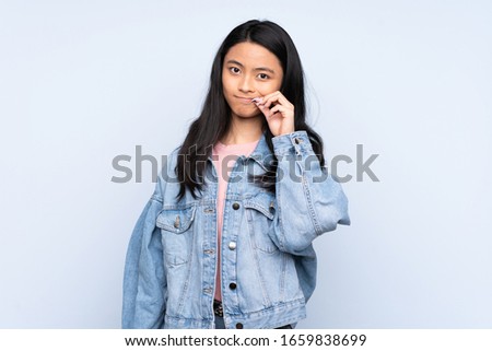 Teenager Chinese woman isolated on blue background showing a sign of silence gesture