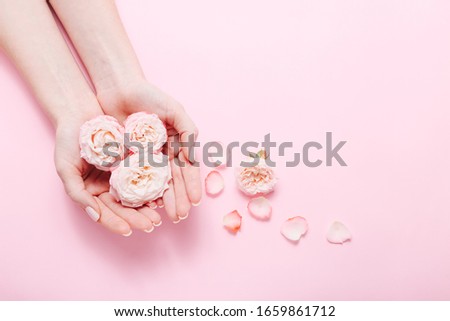 Woman's hands with trendy manicure holding bunch of pink rose on pink background, top view.